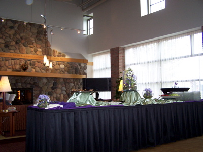 Draped reception tables stand in a bright room with a stone fireplace.