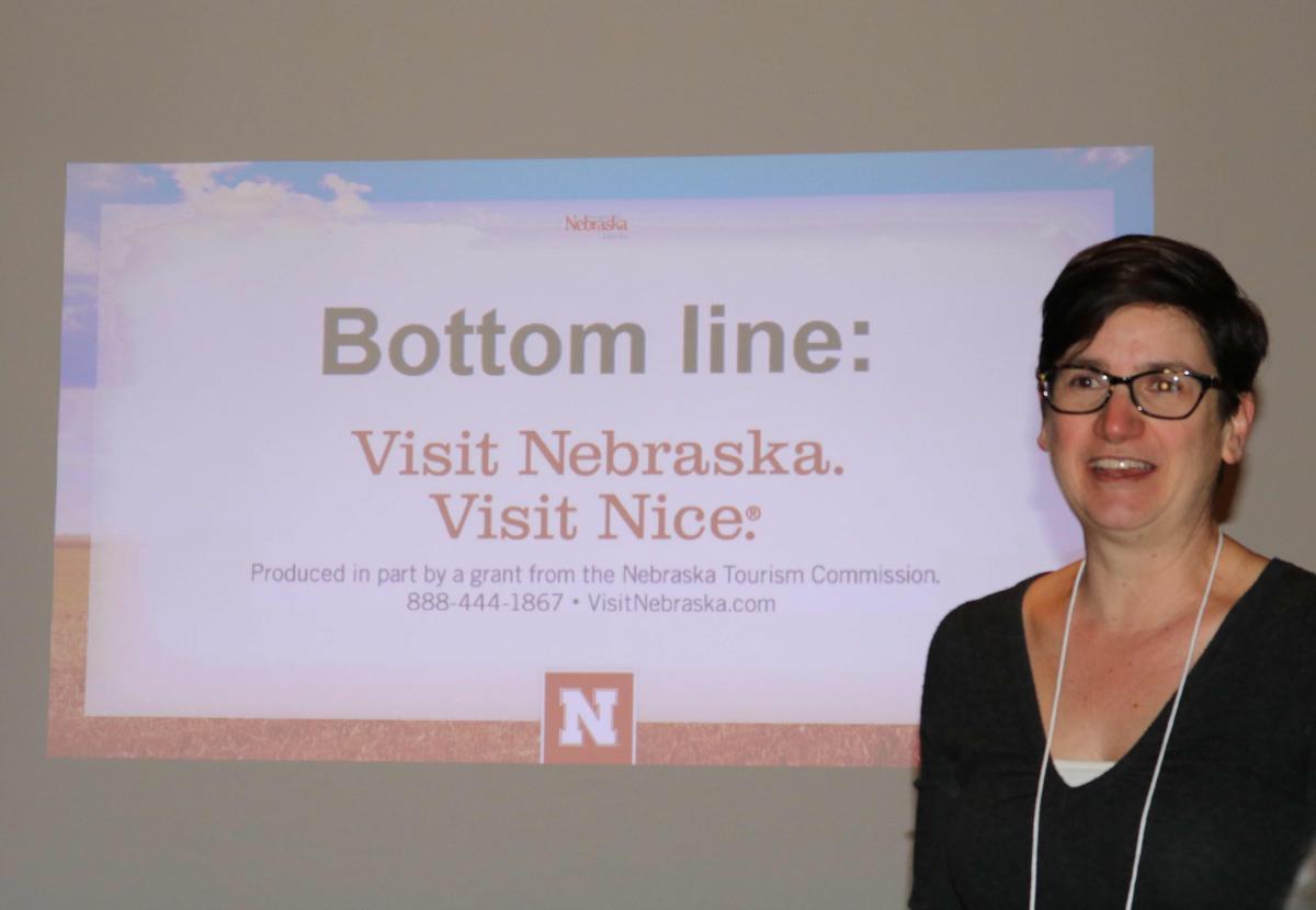 An adult stands beside a projected slide mentioning Nebraska and Nice.