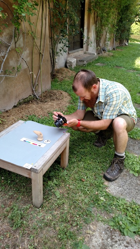 An adult crouches beside a small outdoor table with equipment and an object.