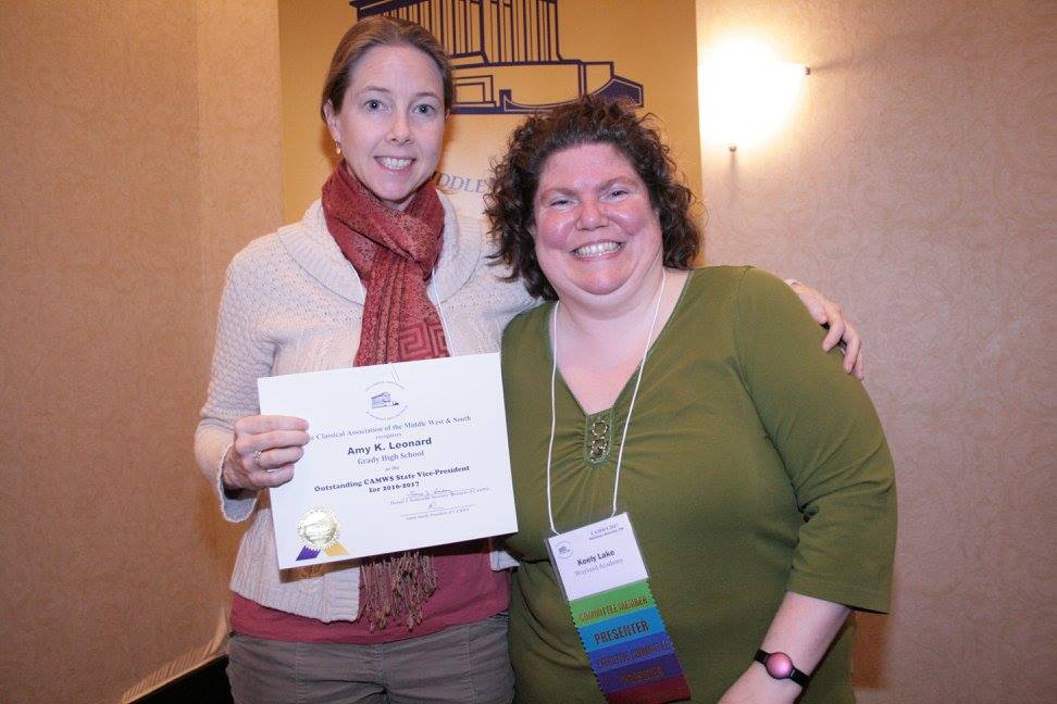 Two adults stand together indoors, one holding a certificate.