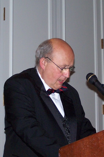 An adult in formal dress reads at a lectern with a microphone.
