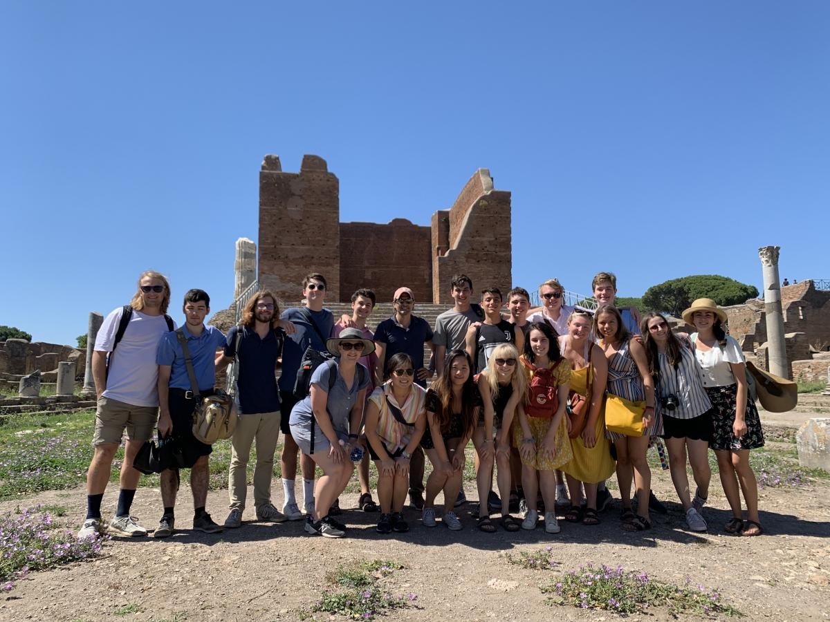A group poses outdoors among stone ruins beneath a blue sky.