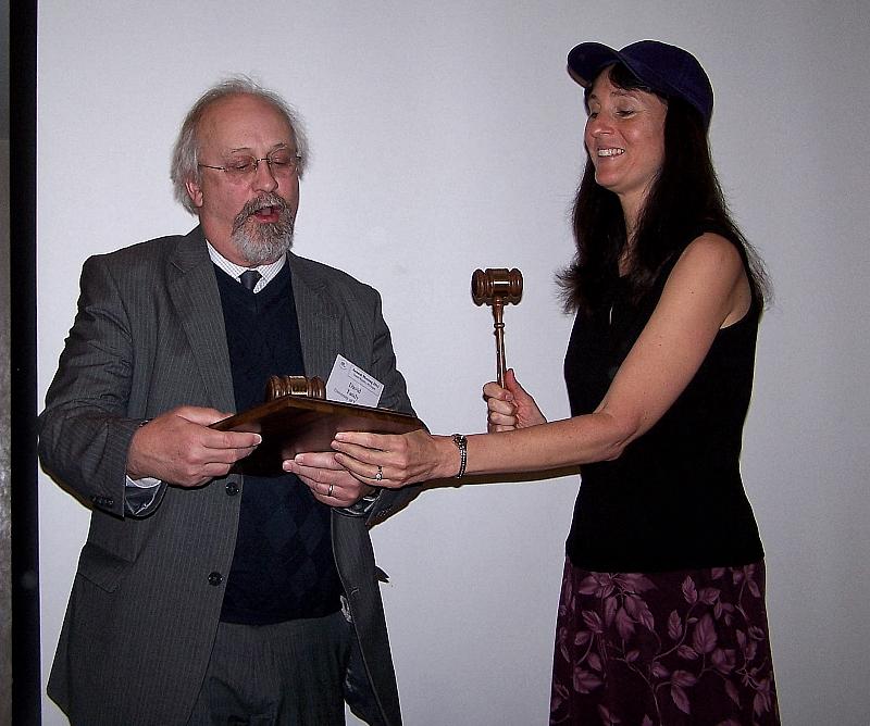 Two adults stand together holding a gavel and wooden board.