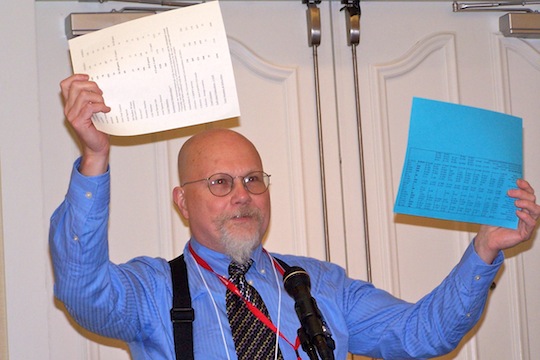 An adult wearing a conference badge holds up two sheets of paper.