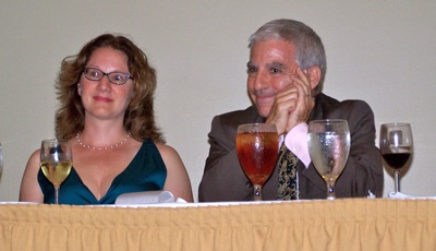Two adults sit at a banquet table with wine glasses.